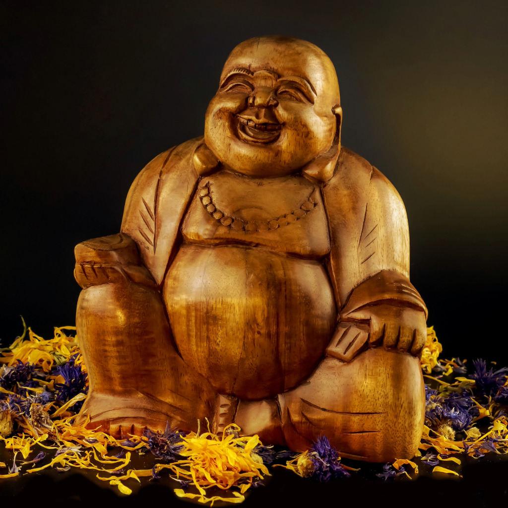Carved wooden Laughing Buddha figurine surrounded by flower petals